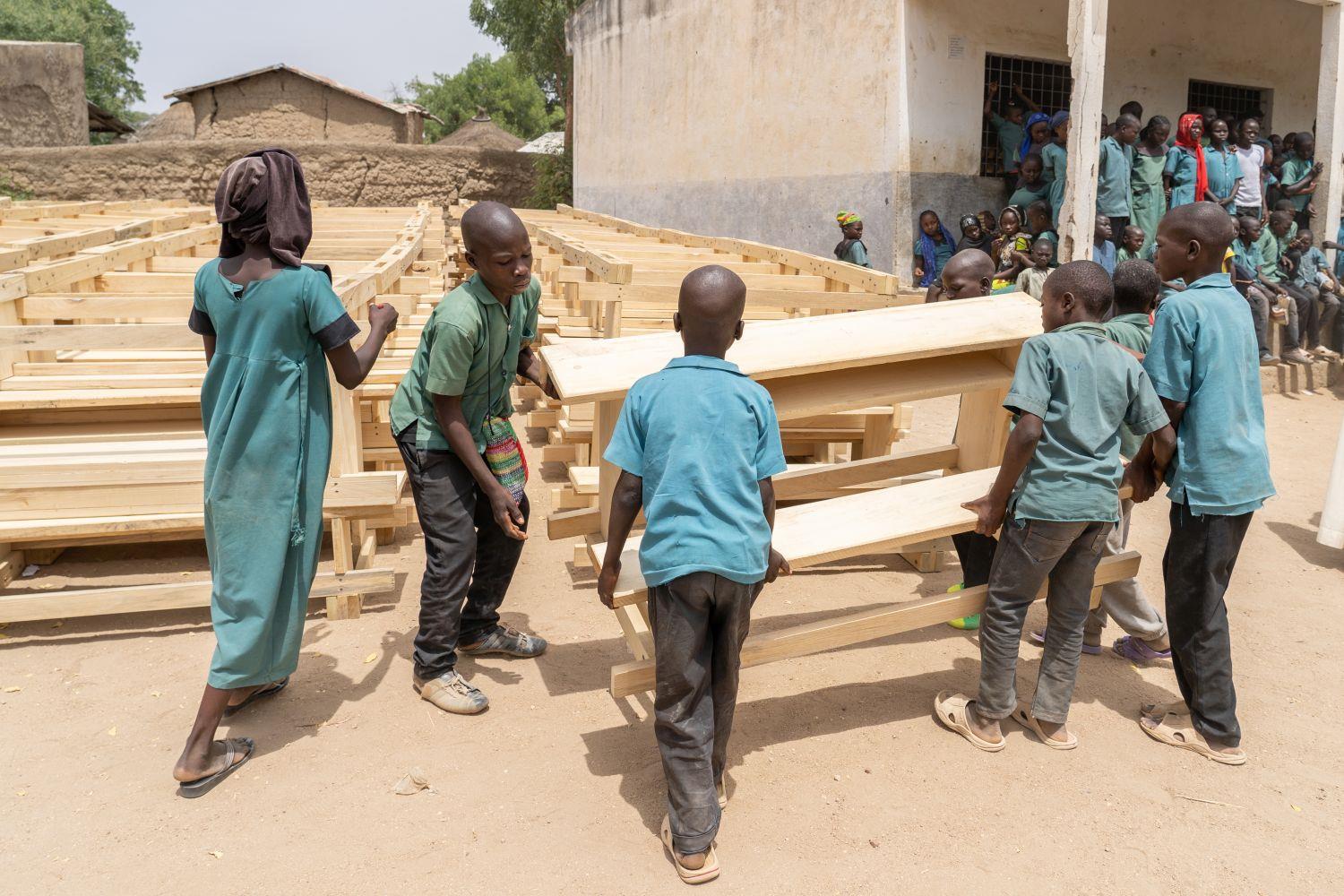 Kamerun: Schulbänke für die Schule in Zamay Kinder tragen eine Schulbank
