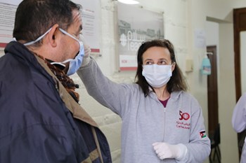 Eine Mitarbeiterin der Caritas Jordanien misst bei einem Patienten Fieber.
