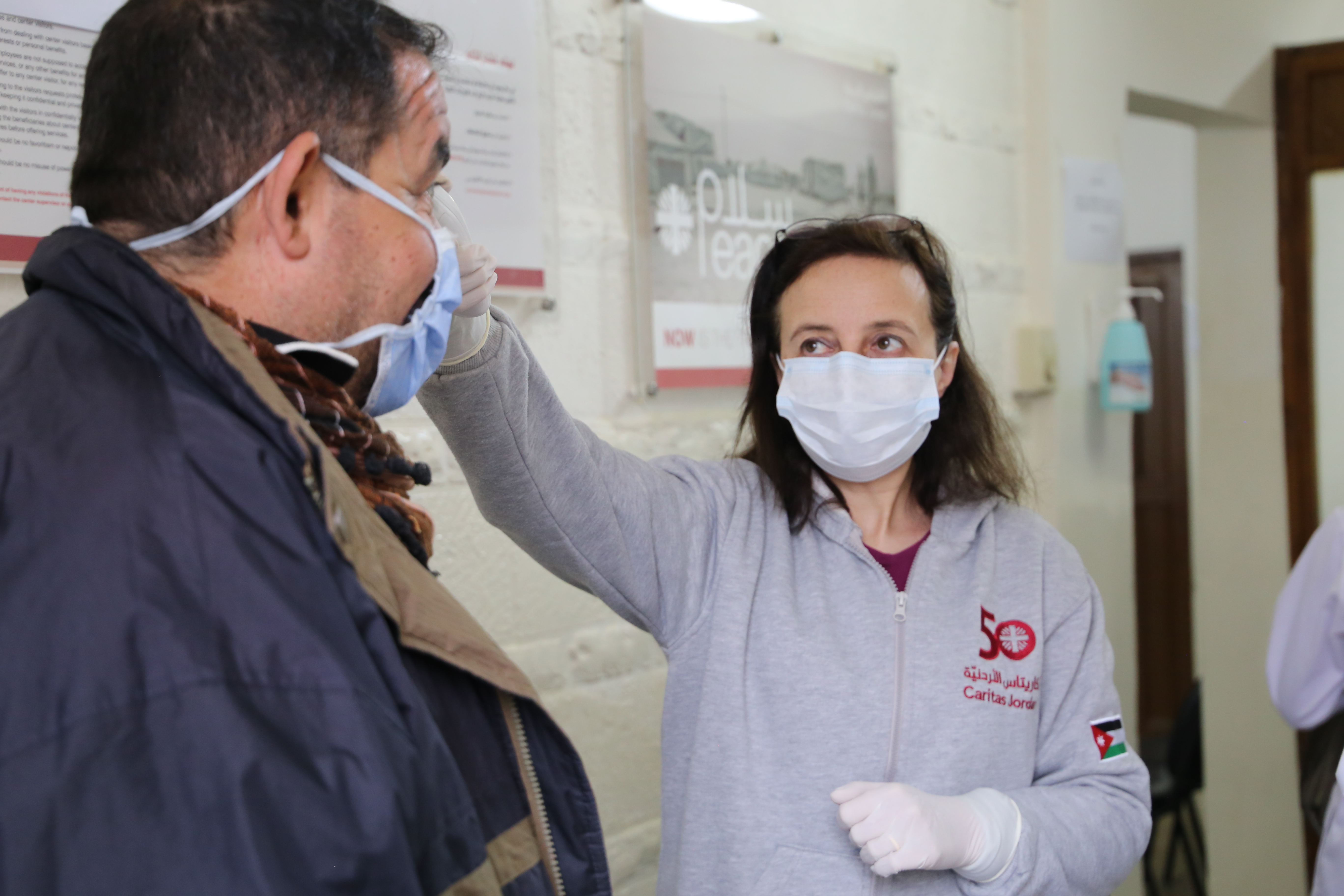 Eine Frau mit Mundschutz mist Fieber bei einem Mann mit Mundschutz.